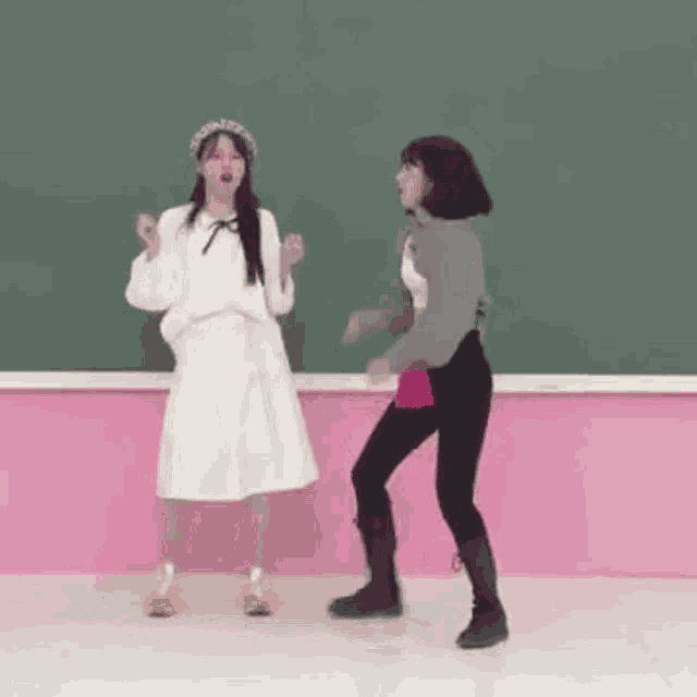 two young women are dancing in front of a blackboard in a classroom .