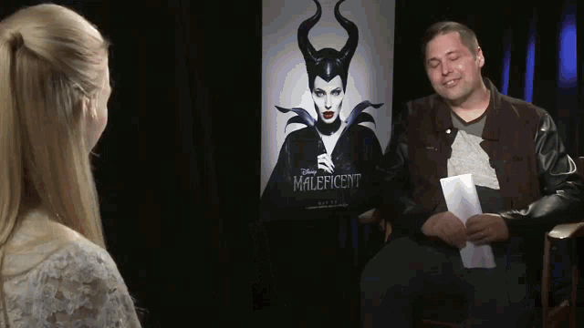 a man and a woman are sitting in front of a poster for maleficent