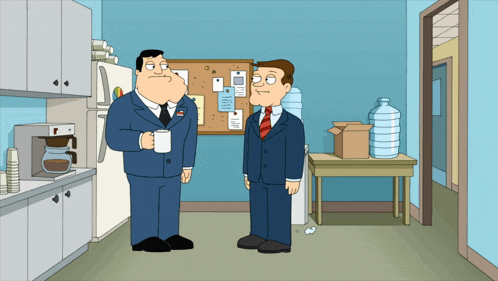two men in suits and ties are standing in a kitchen talking to each other