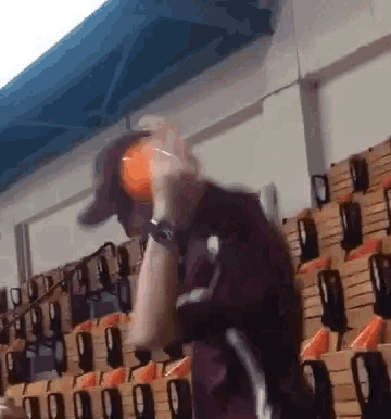 a man in a maroon jacket is holding an orange ball in front of a row of wooden seats