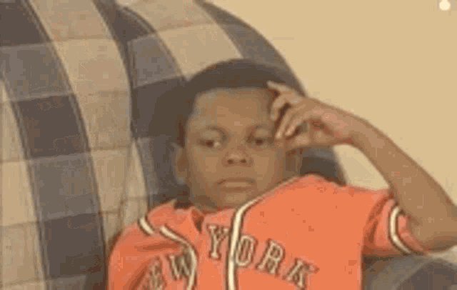 a young boy is sitting on a couch wearing a new york shirt .
