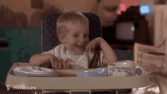 a baby is sitting in a high chair eating cereal and laughing .