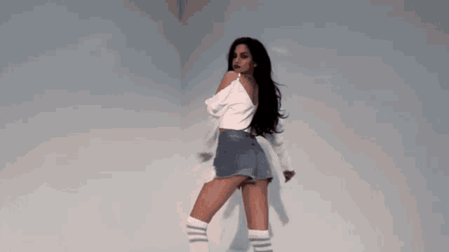 a woman is dancing in a room wearing knee high socks and denim shorts .
