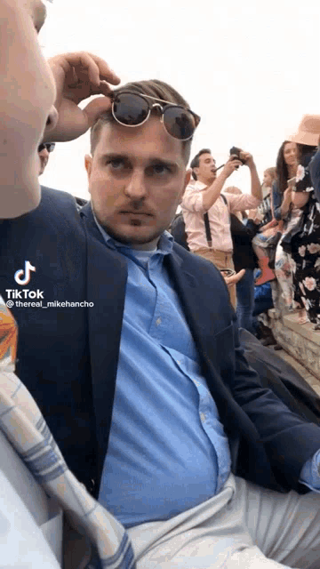 a man wearing sunglasses and a blue shirt is sitting in front of a crowd with a tiktok watermark