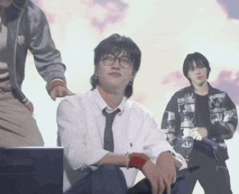 a man in a white shirt and tie is sitting in front of a laptop computer while two other men are dancing in the background .