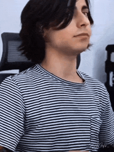 a young man with long hair is wearing a striped shirt and sitting in an office chair .