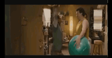 a man in a yellow tank top is holding a large blue exercise ball