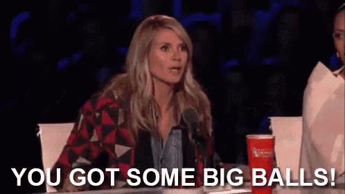 a woman is sitting at a table with a microphone in front of her and the words `` you got some big balls '' .