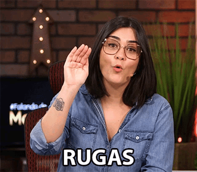 a woman wearing glasses and a denim shirt has the word rugas on her chest