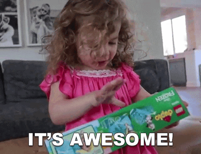 a little girl is holding a lego box and says it 's awesome !