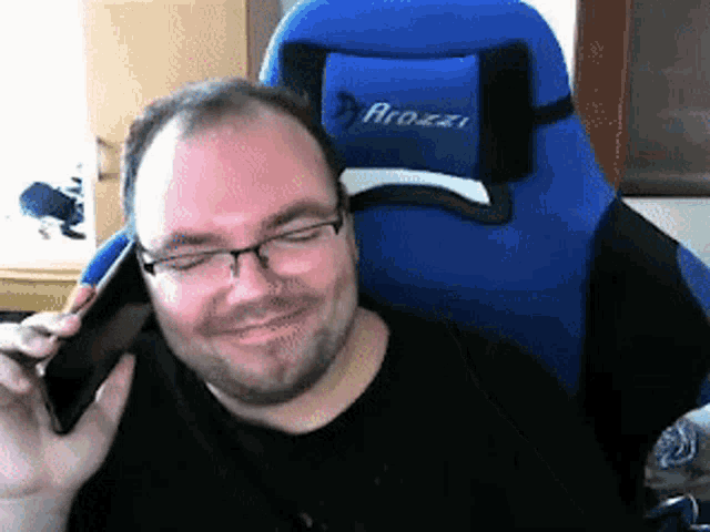 a man is sitting in a blue arozai chair talking on his phone