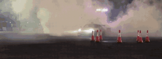 a car is drifting on a track at night and smoke is coming out of the car .