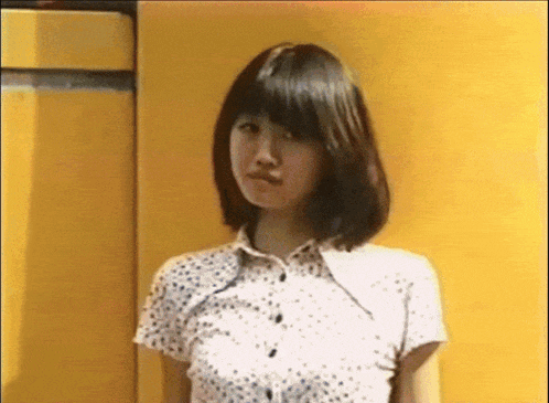 a woman wearing a white shirt with polka dots is standing in front of a yellow wall .