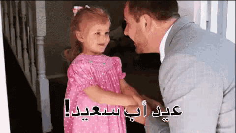 a little girl in a pink dress is holding hands with a man in a suit .