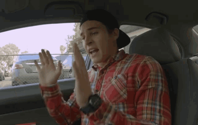 a man wearing a plaid shirt and a black hat is sitting in the back seat of a car