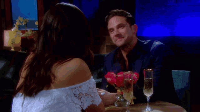 a man and woman are sitting at a table with glasses of champagne