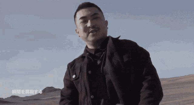 a man in a black jacket stands in front of a desert landscape