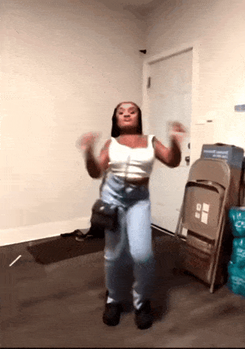 a woman is dancing in a room with a stack of folding chairs behind her