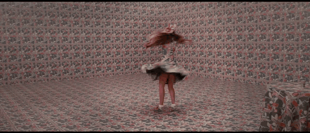 a woman in a dress is dancing in front of a wall that has a pattern of hearts