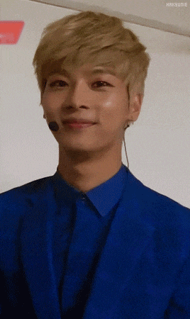 a young man wearing a blue suit and a blue shirt with a microphone in his ear is smiling