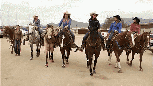 a group of women are riding horses in a line on a dirt road