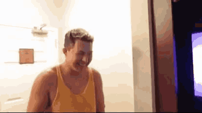 a man in a yellow tank top is laughing while standing in a room .