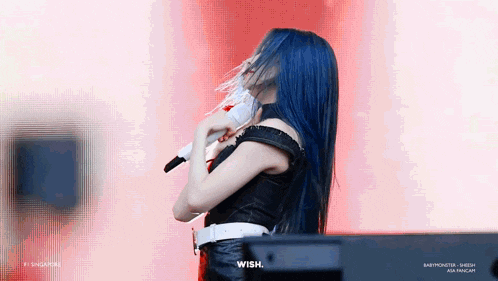 a woman with blue hair is holding a microphone and dancing on stage .