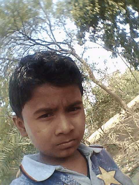 a young boy wearing a blue shirt with a yellow star on it looks at the camera