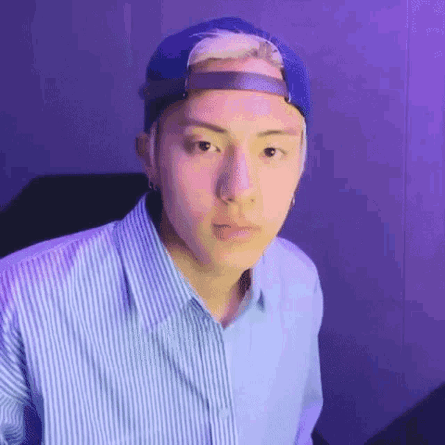 a young man wearing a blue baseball cap and a blue striped shirt is looking at the camera .
