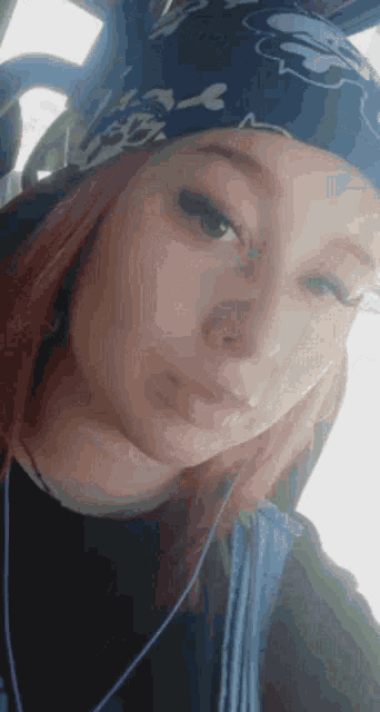 a young woman wearing a bandana and a hat is taking a selfie .