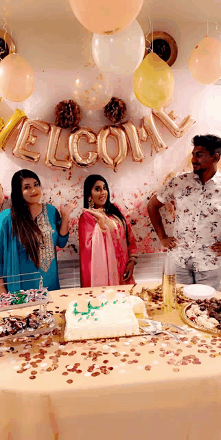 a group of people standing around a table with balloons and a sign that says welcome