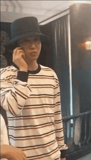 a man wearing a black hat and a striped shirt is talking on a cell phone .