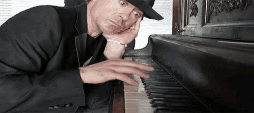 a man in a tuxedo and fedora is playing a piano