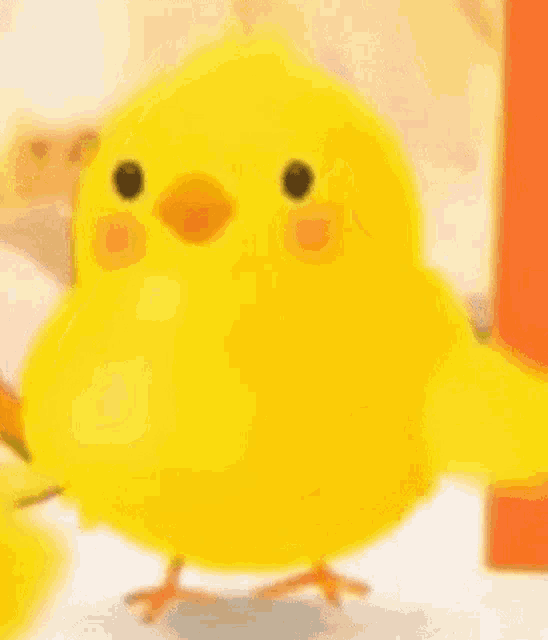 a yellow chicken with a red beak is standing on a table next to a bottle of ketchup .