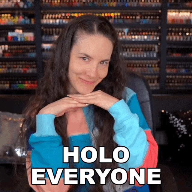 a woman in a colorful sweater has her hands on her chin and says holo everyone