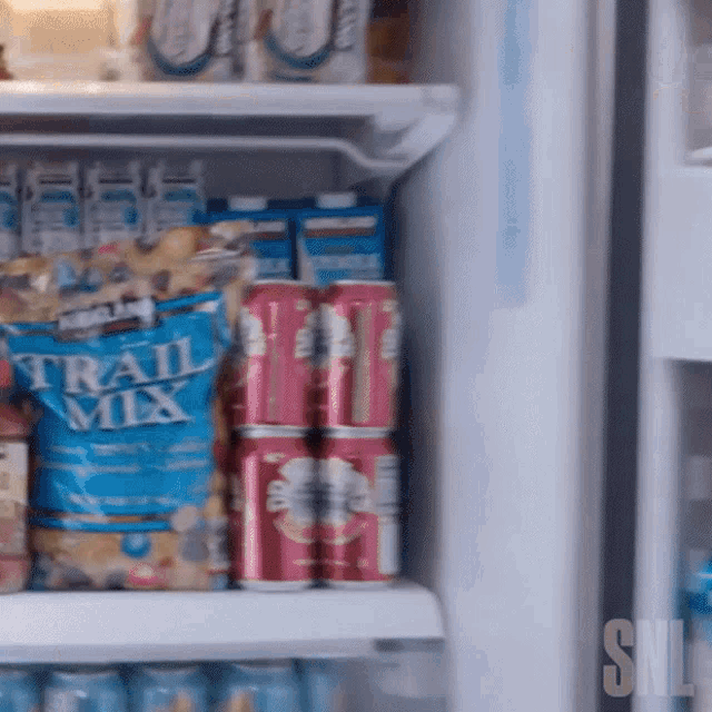 a bag of kirkland trail mix sits on a refrigerator shelf next to cans of soda