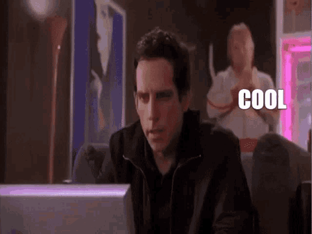 a man is sitting in front of a computer and the word cool is written on the screen .