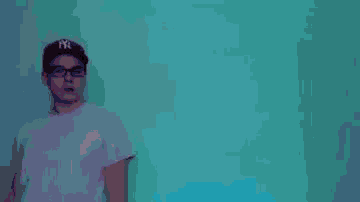 a man wearing glasses and a white t-shirt is standing in front of a blue background .
