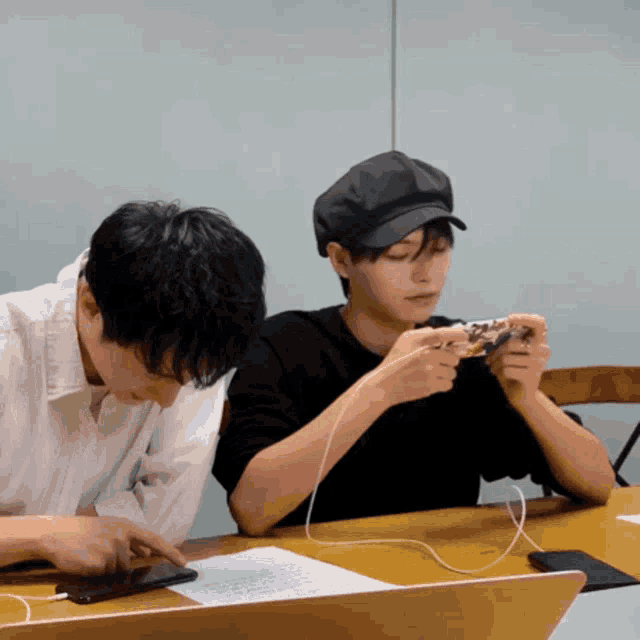 two men are sitting at a table playing a game on their phones