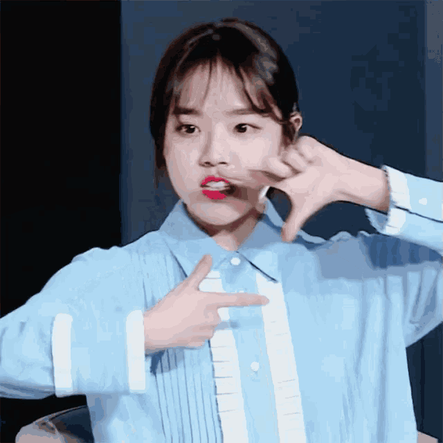 a girl in a blue shirt is making a funny face with her hands
