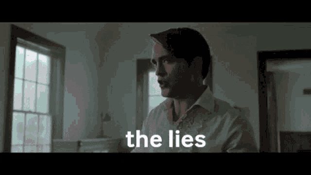 a man in a white shirt is talking to another man in a dark room .