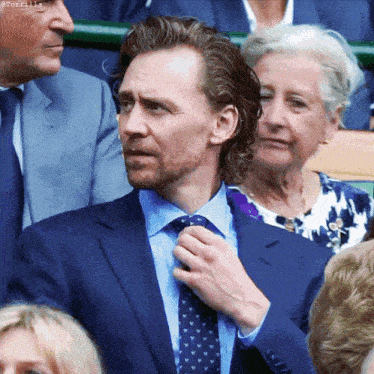a man in a suit and tie adjusts his tie while sitting in a crowd