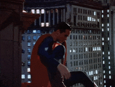 a man in a superman costume is kneeling down in front of a building