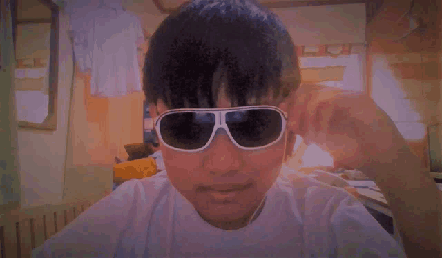a young man wearing sunglasses and a white shirt looks at the camera