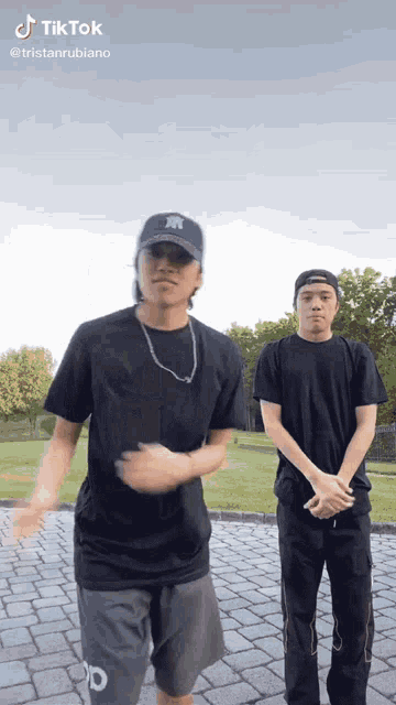 two young men are dancing on a brick walkway . one of the men is wearing a new york yankees hat .
