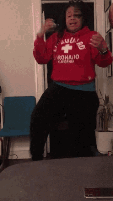 a woman in a red lifeguard sweatshirt is dancing in a room
