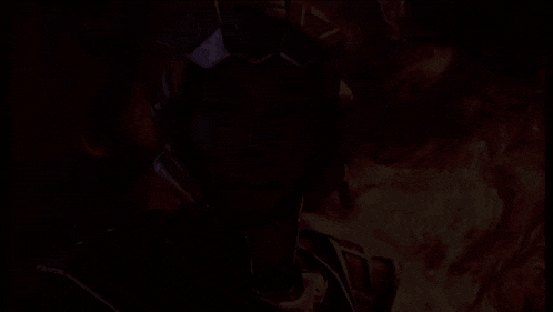 a woman in a futuristic armor is standing in front of a fire .