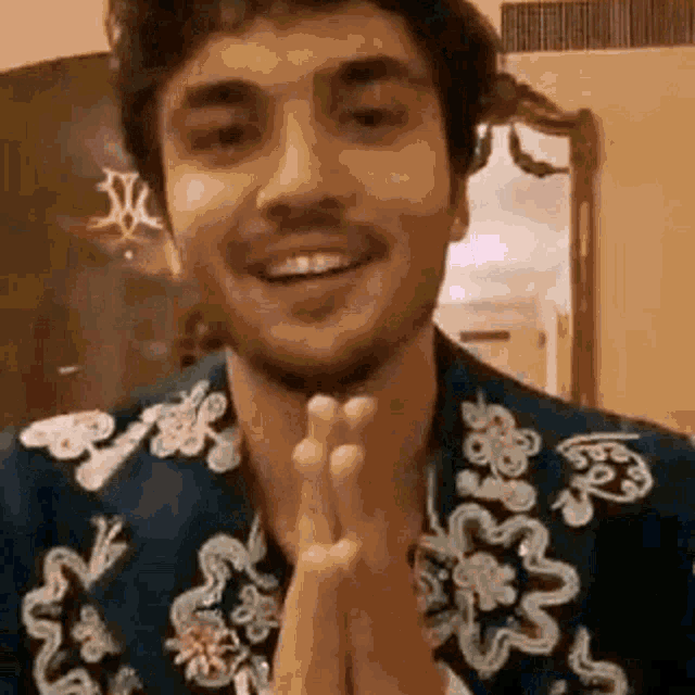a man wearing a blue jacket with a floral pattern is smiling and holding his hands together .