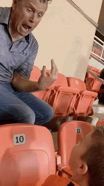 a man in an under armour shirt sits in a stadium talking to a boy