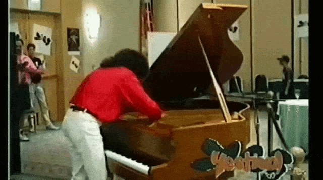 a man in a red shirt is playing a piano with the lid open .